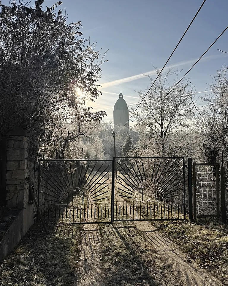 Eisentor mit Sonnenstrahlen-Muster im Raureif, dahinter der Weg und der Dicke Wilhelm, Dezember 2025